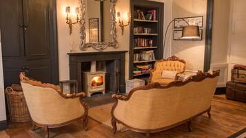 Un salon chaleureux avec une cheminée, deux fauteuils rembourrés, une bibliothèque et un grand miroir décoratif.