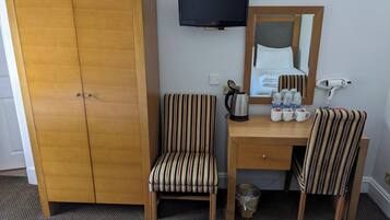 Une chambre d’hôtel avec une armoire en bois, un bureau avec deux chaises à rayures, une télévision, un miroir et un sèche-cheveux.