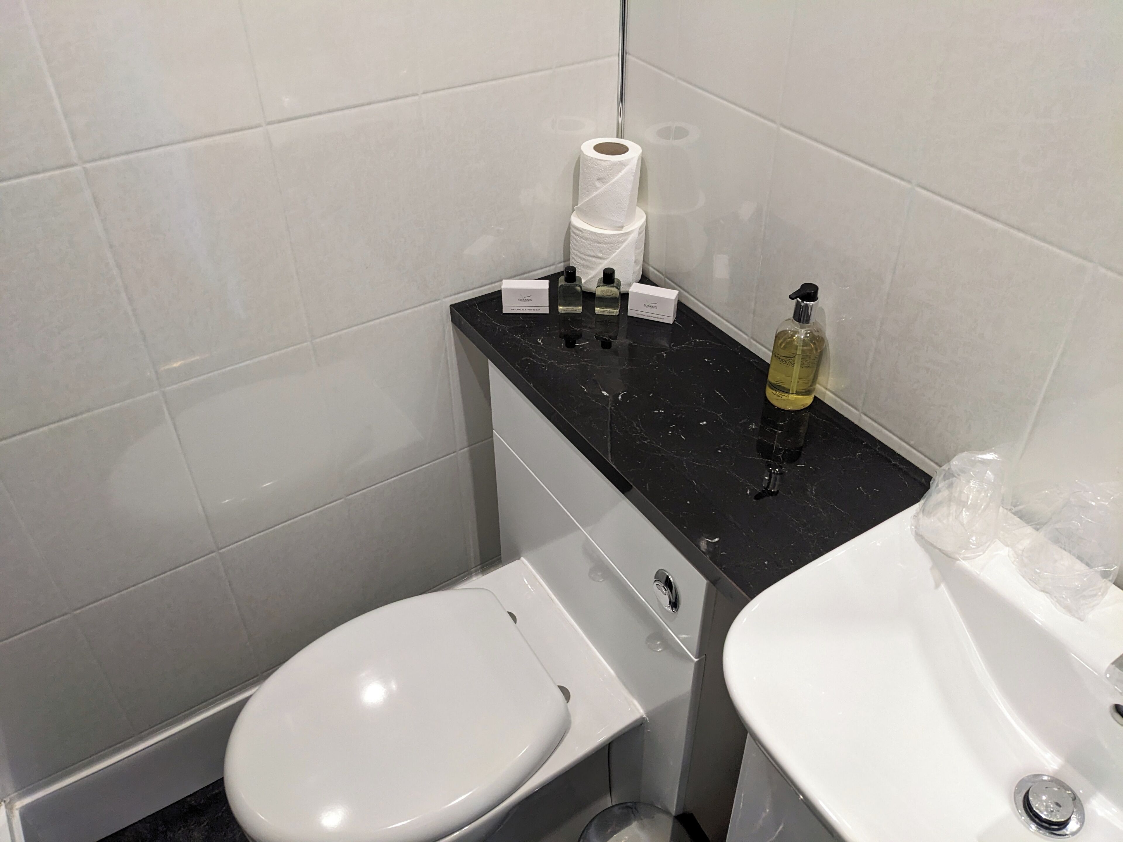 Un baño con inodoro blanco, lavamanos de mármol negro y un espejo.