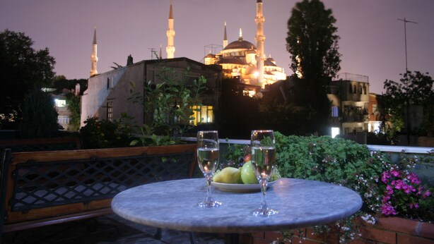 A table with two glasses and a plate of fruit, set against a backdrop of a mosque with illuminated minarets. - Dersaadet Hotel - Special Class (Istanbul)