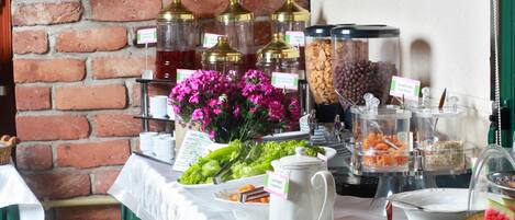 A buffet setup with various food items, a pitcher, and a plant on a brick wall backdrop.