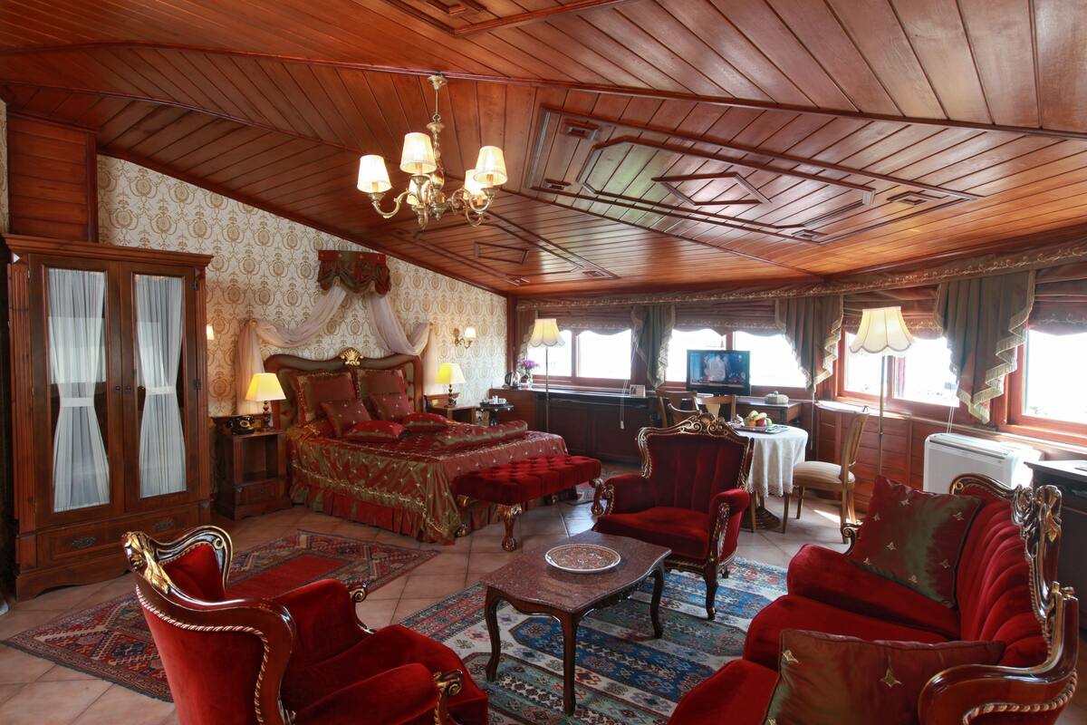 A traditional room with a large bed, red upholstered furniture, a chandelier, and a wooden ceiling.