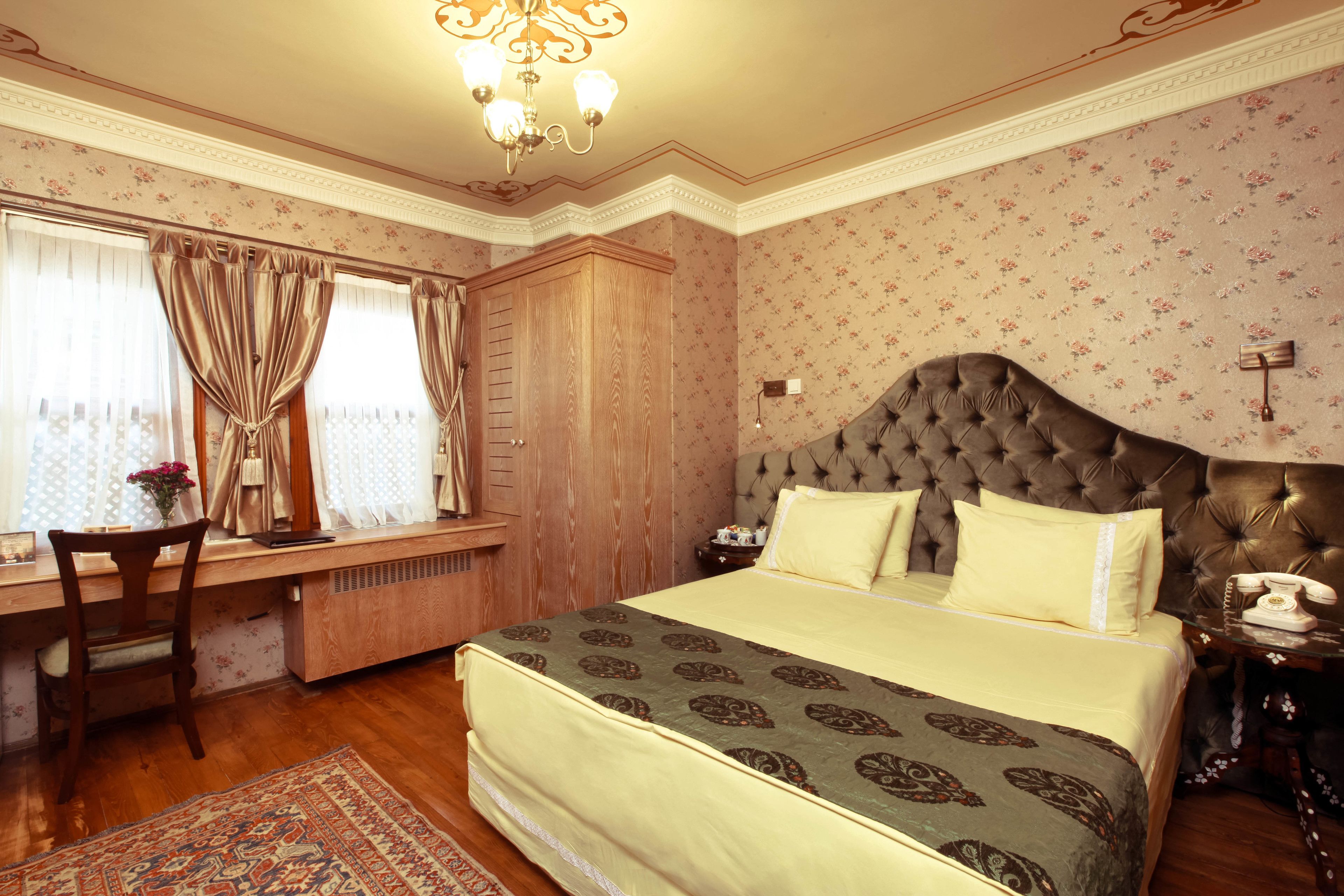 Een slaapkamer met een groot bed, een houten bureau, een stoel, een kroonluchter en een raam met gordijnen.