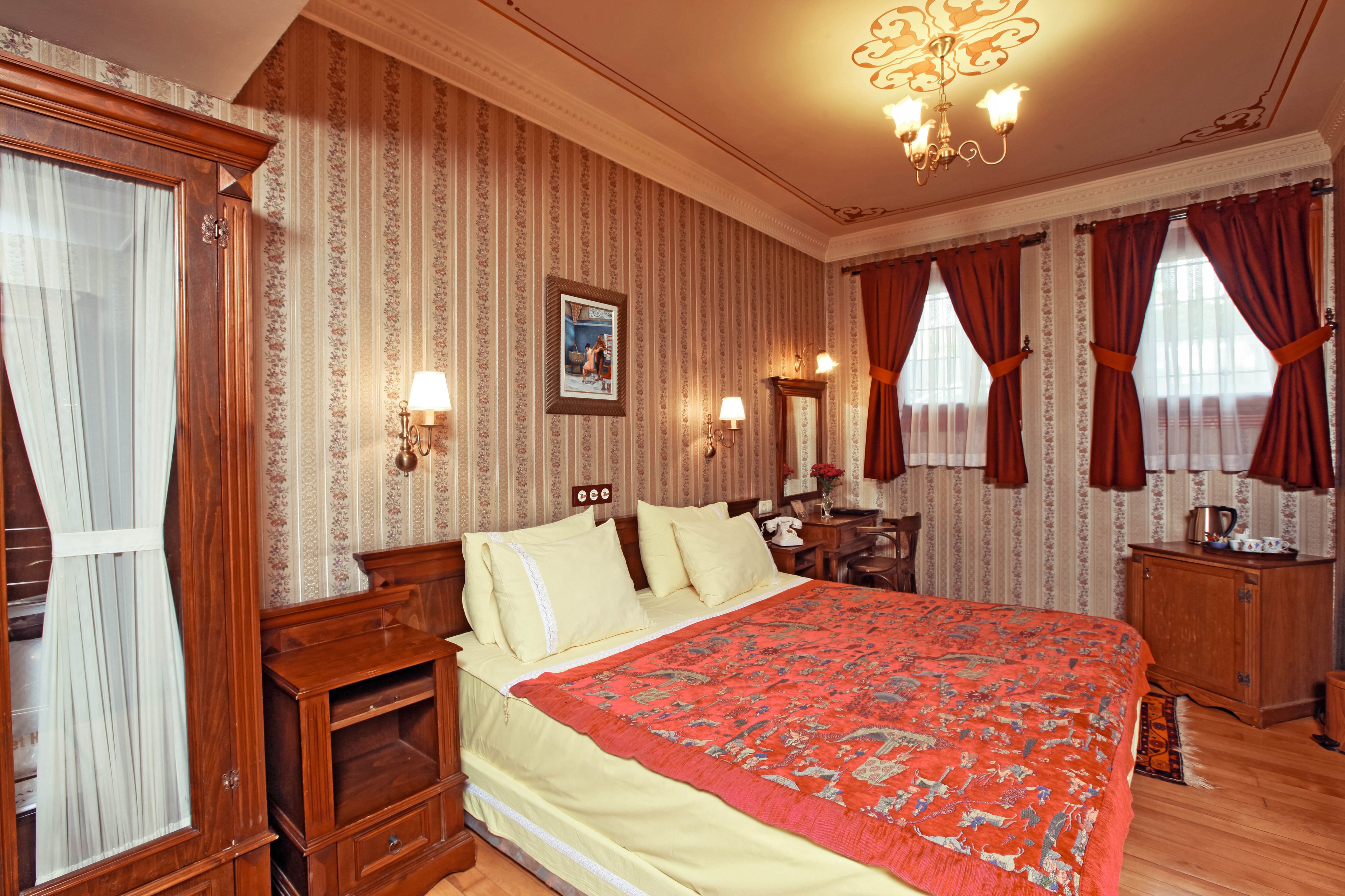 A traditional room with a large bed, wooden furniture, a chandelier, and striped wallpaper.