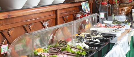 Un bufé con diversas opciones de comida, entre ellas ensaladas, frutas y bebidas.