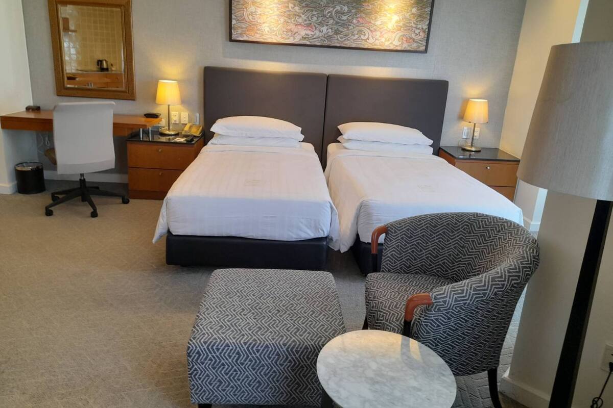 Ein Hotelzimmer mit zwei Betten, einem Schreibtisch, einem Stuhl, einem kleinen Tisch und einem Bild an der Wand.