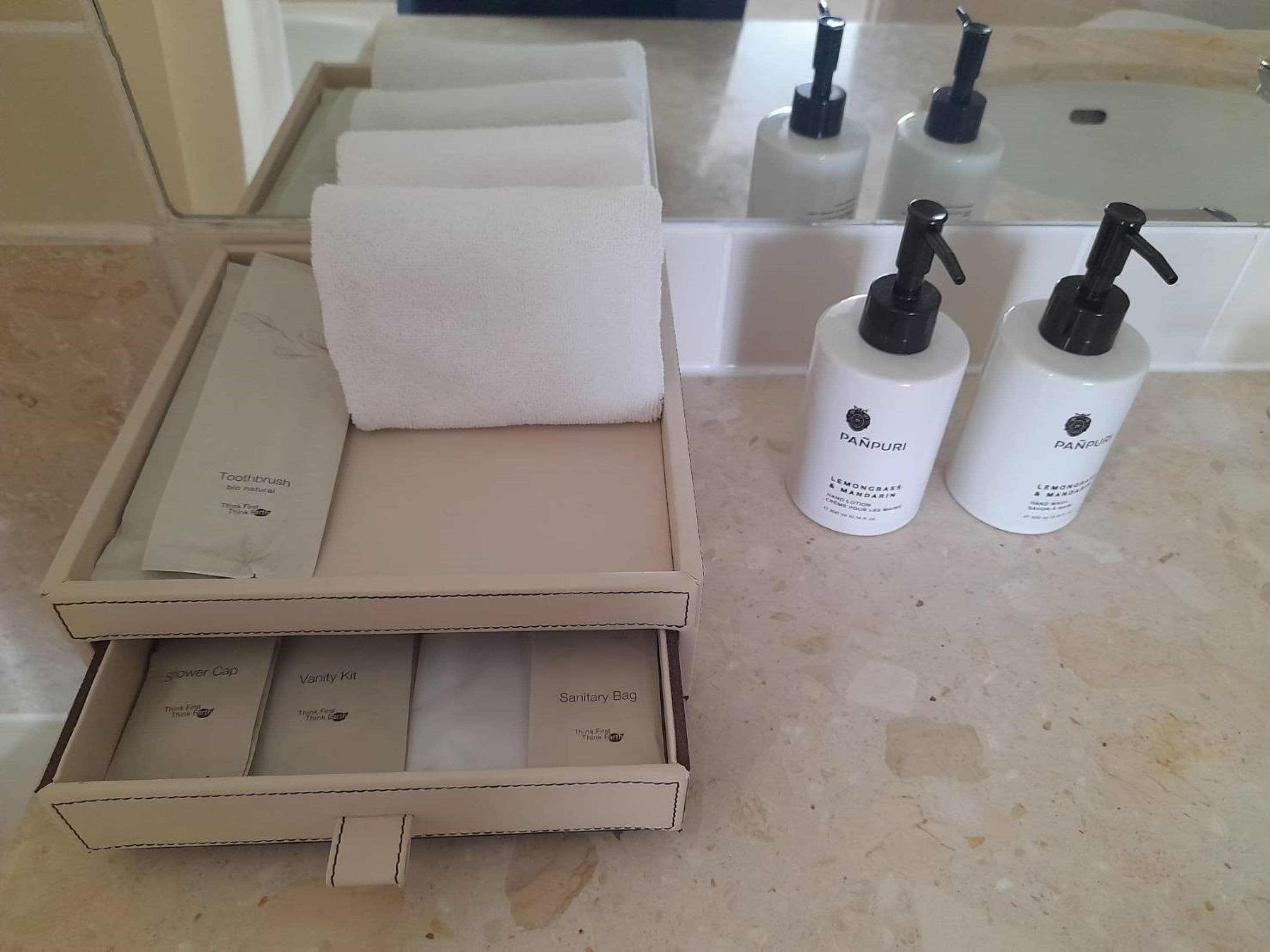 Une salle de bain équipée d’un porte-serviettes, de deux flacons de gel hydroalcoolique et d’une boîte contenant un bonnet de douche, une trousse de toilette et un sac hygiénique.