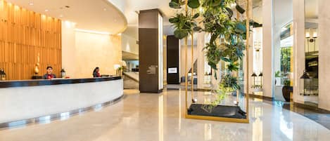 Un moderno vestíbulo de hotel con un mostrador de recepción curvo, una escalera y una planta de interior grande.