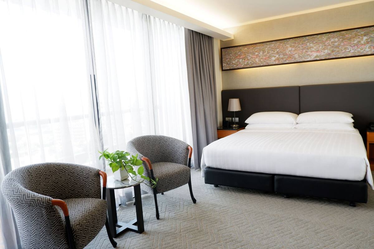 Ein Hotelzimmer mit einem großen Bett, zwei Sesseln, einem kleinen Tisch mit Pflanze und einem Nachttisch mit Lampe.