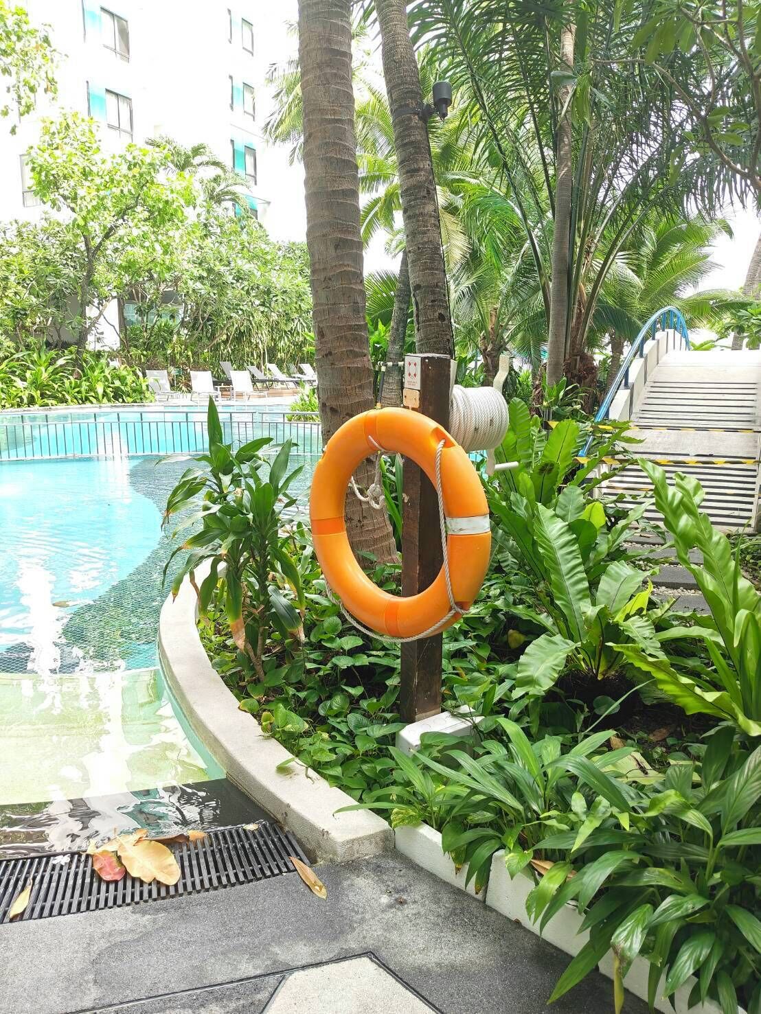 Ein Poolbereich mit einem Rettungsring, Palmen und einem Gebäude im Hintergrund.