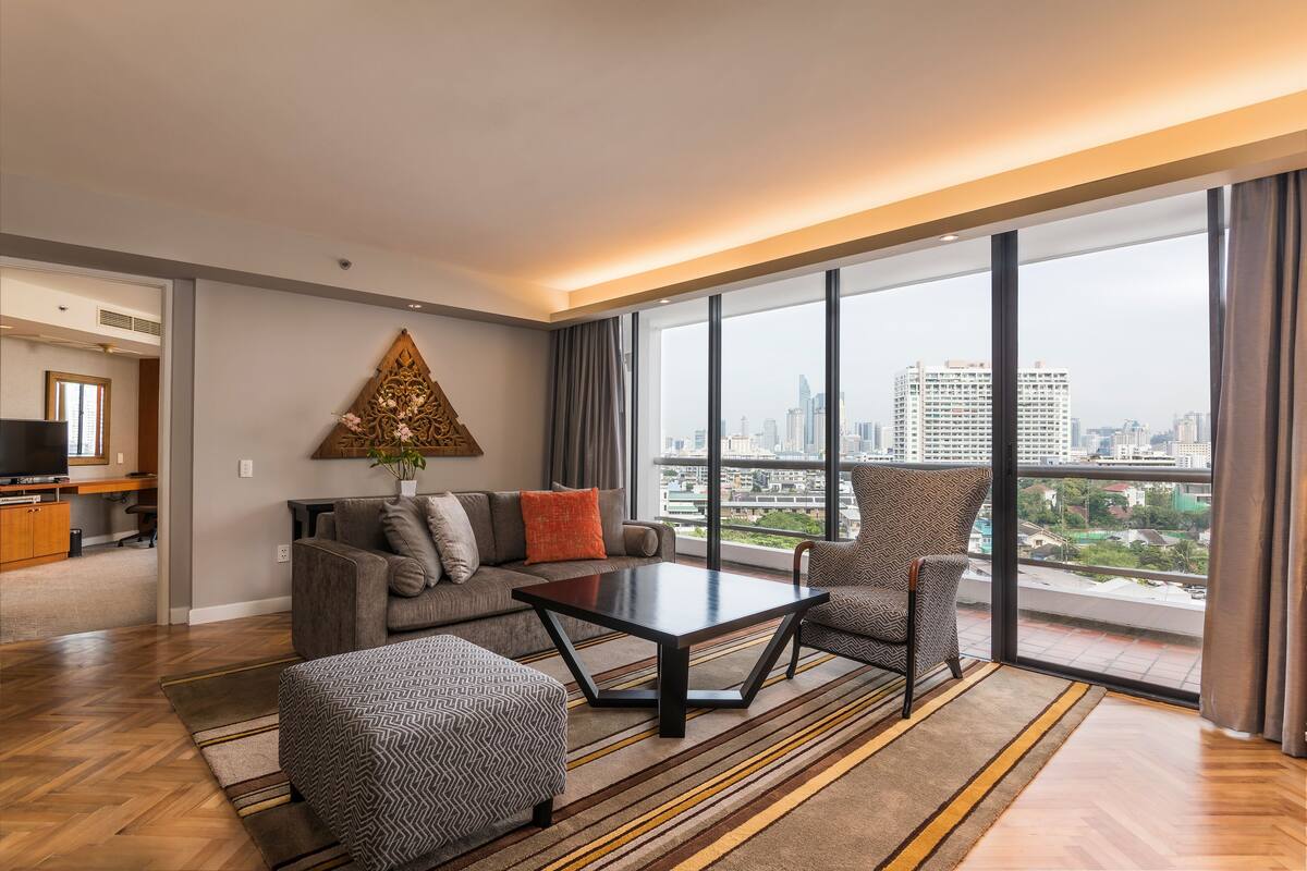 Ein modernes Hotelzimmer mit großem Fenster, einer Couch, einem Couchtisch und einem kleinen Hocker.