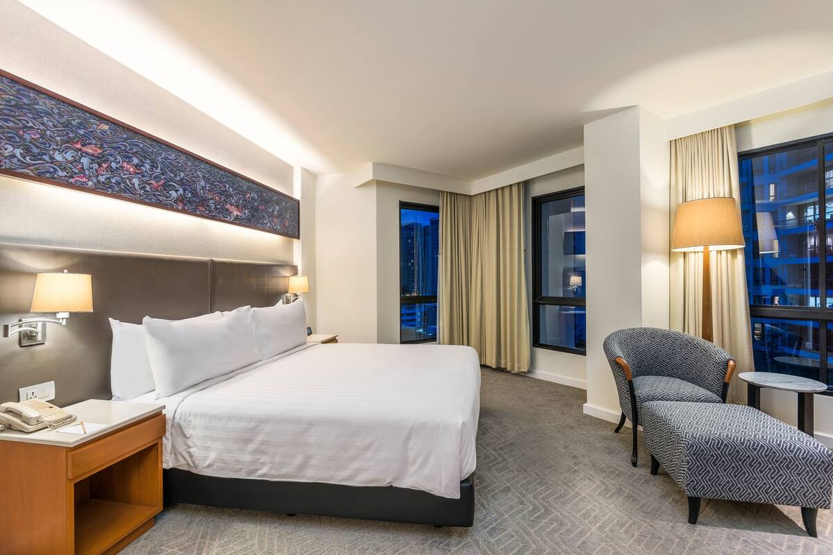 Ein Hotelzimmer mit einem großen Bett, einem Nachttisch mit Lampe, einem Sessel und einem kleinen Tisch.