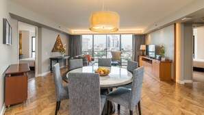 Una habitación de hotel moderna con una mesa de comedor redonda, sillas tapizadas en gris, un escritorio de madera y vistas a la ciudad.