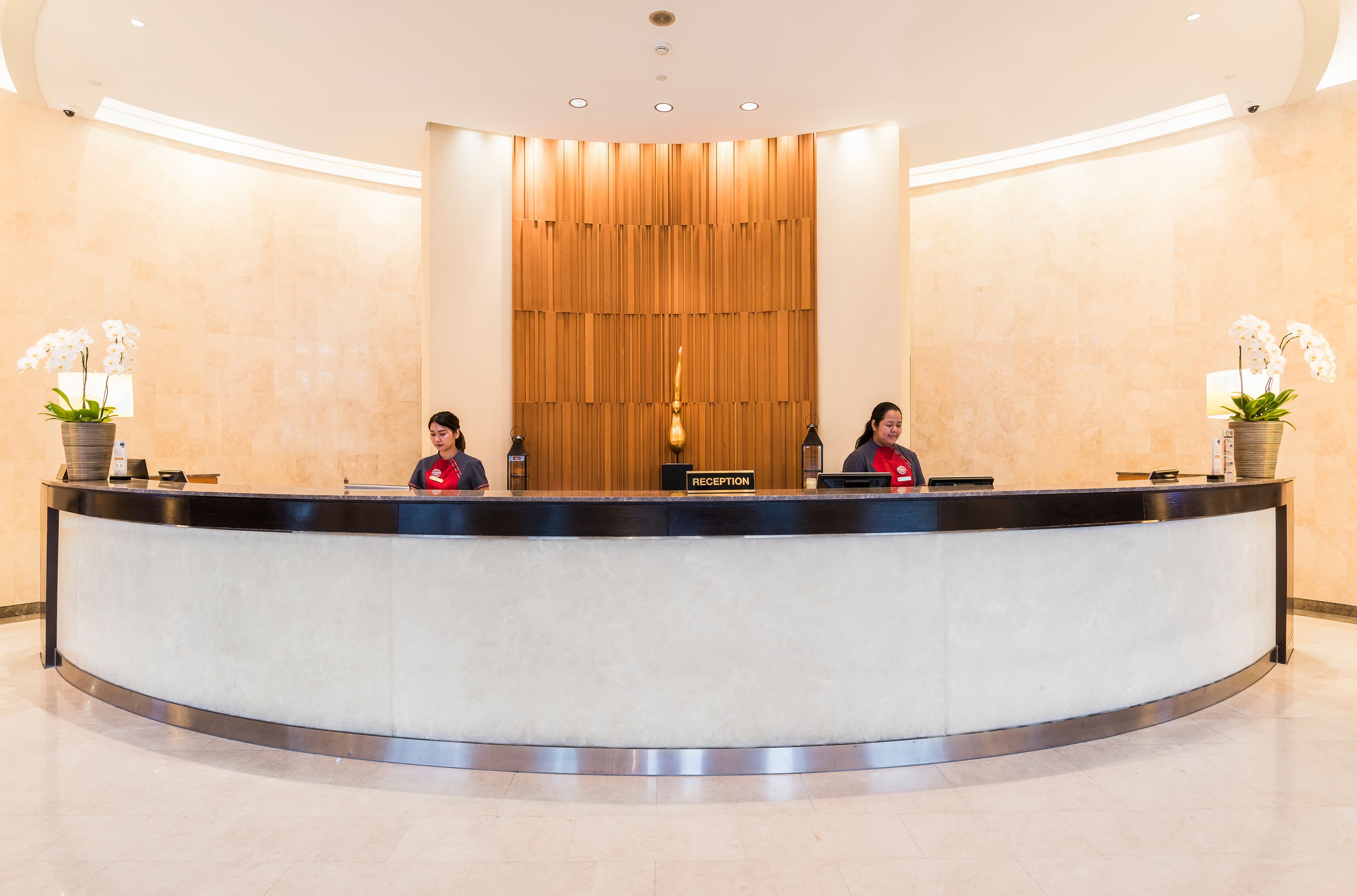 A reception desk with a wooden backdrop and potted orchids.