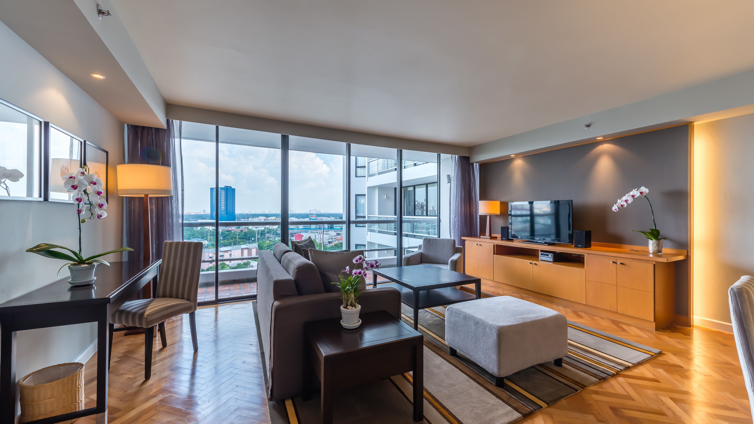 Ein modernes Hotelzimmer mit großem Balkon, einer Couch, einem Esstisch und einem Fernseher.