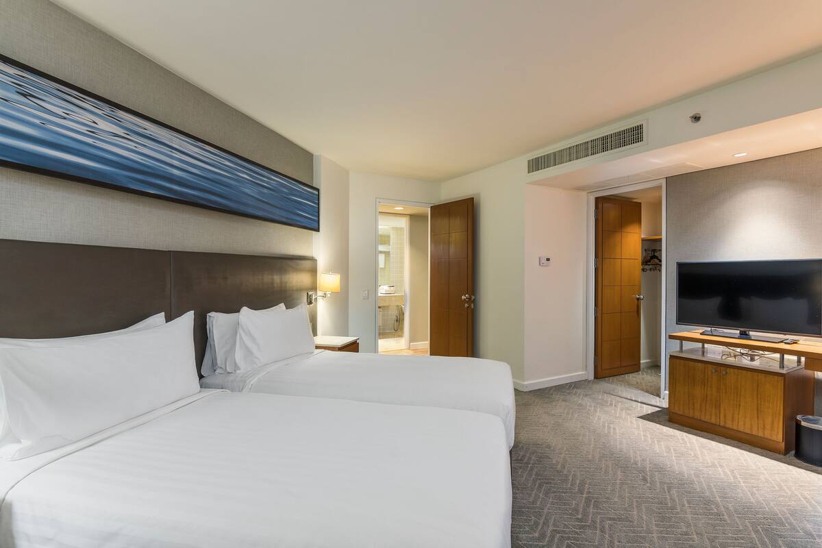 Ein Hotelzimmer mit zwei Betten, einem Fernseher, einer Holzkommode und einem Bild an der Wand.