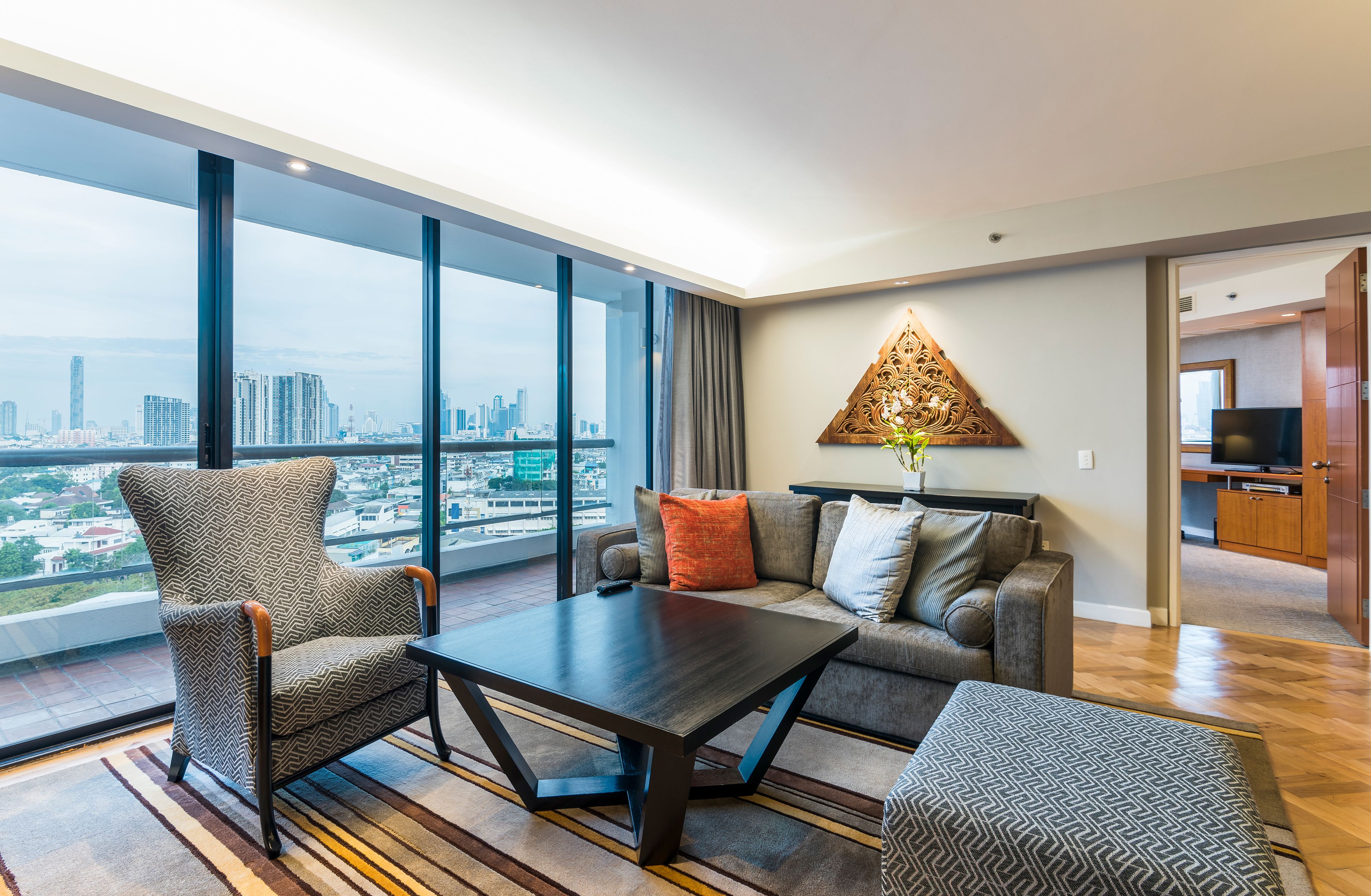 A modern living room with a large window, a sofa, a coffee table, and a decorative wall piece.