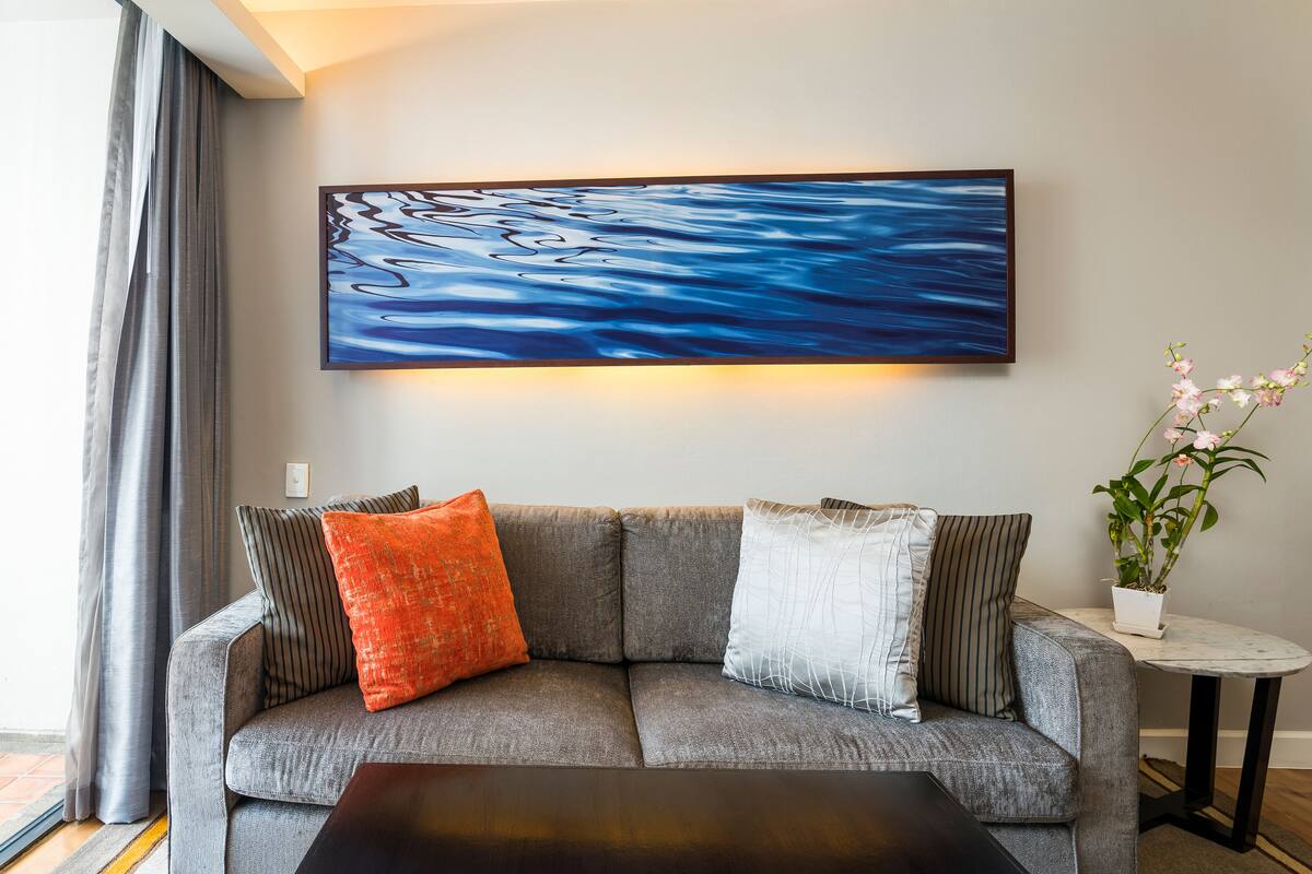 Ein modernes Wohnzimmer mit einem grauen Sofa, einem schwarzen Couchtisch und einem großen, abstrakten Gemälde an der Wand.