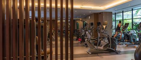 A gym with various exercise machines, a staircase, and large windows with a view of greenery.