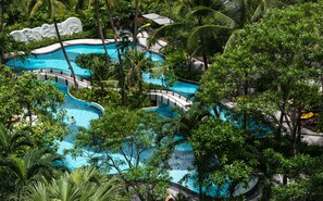 Una piscina amplia y serpenteante rodeada de abundante vegetación y palmeras.