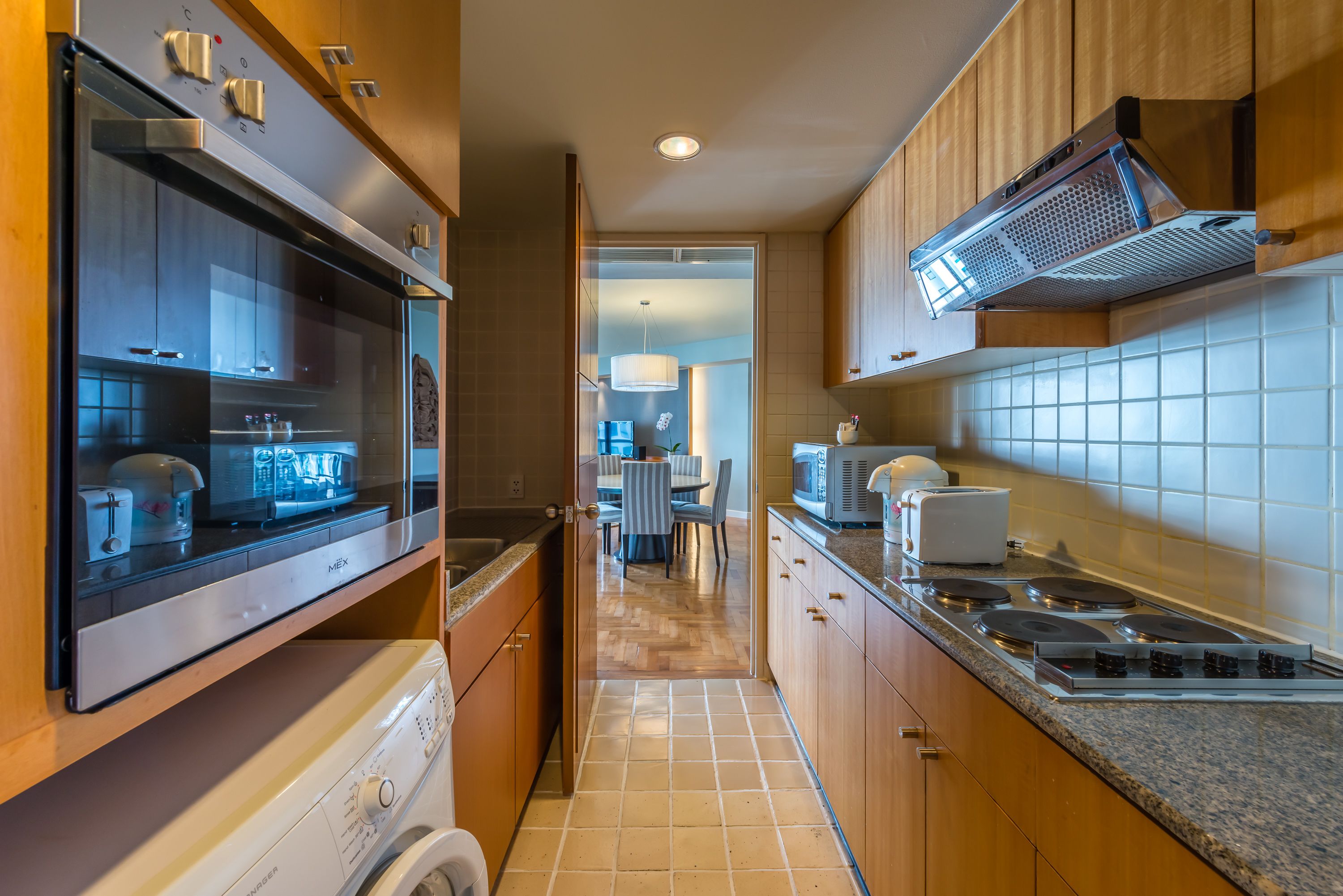 A modern kitchen with wooden cabinets, a built-in oven, a microwave, and a washing machine.