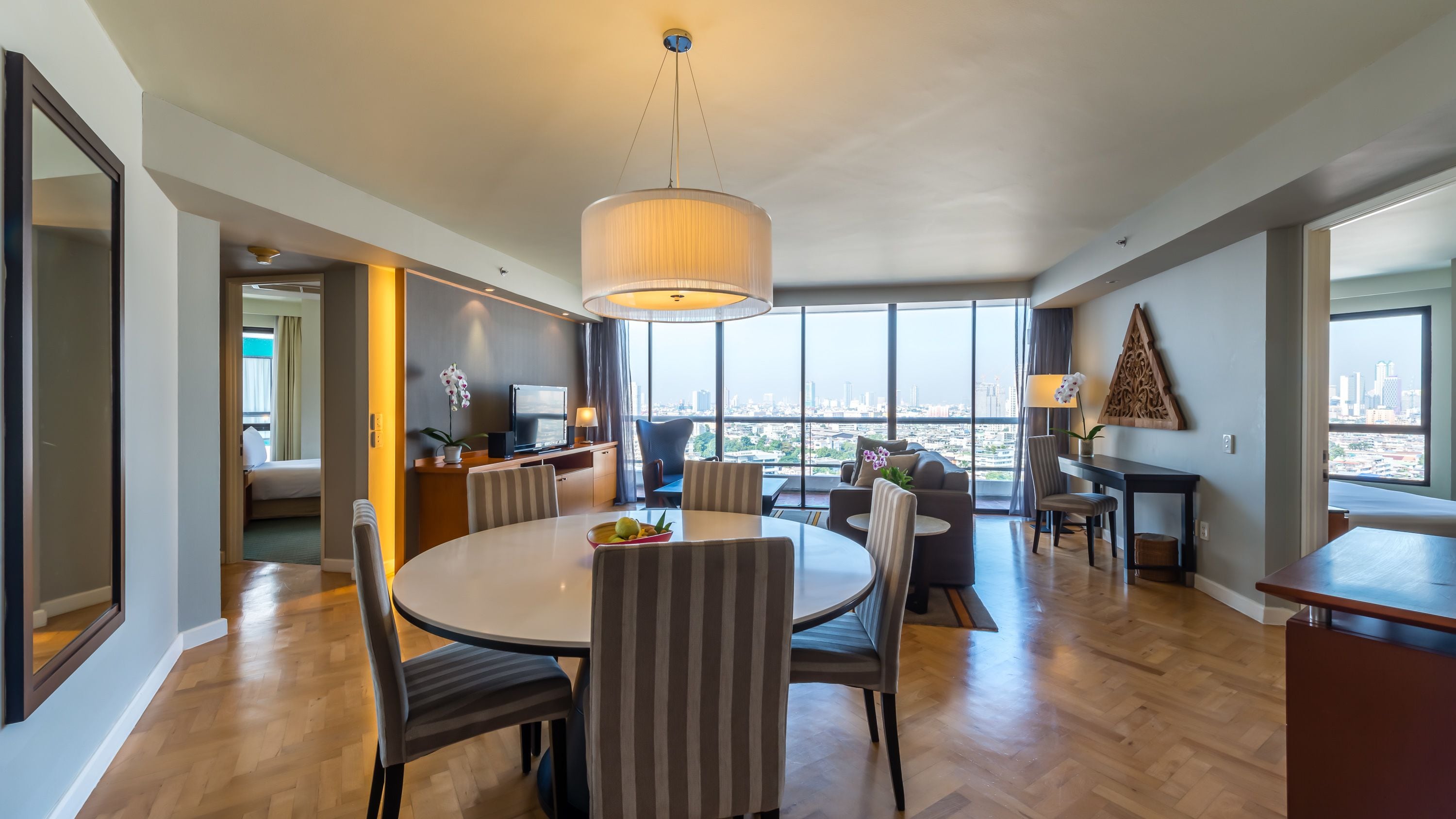 Una habitación de hotel moderna con comedor, un amplio ventanal con vista a la ciudad y una zona de estar acogedora.