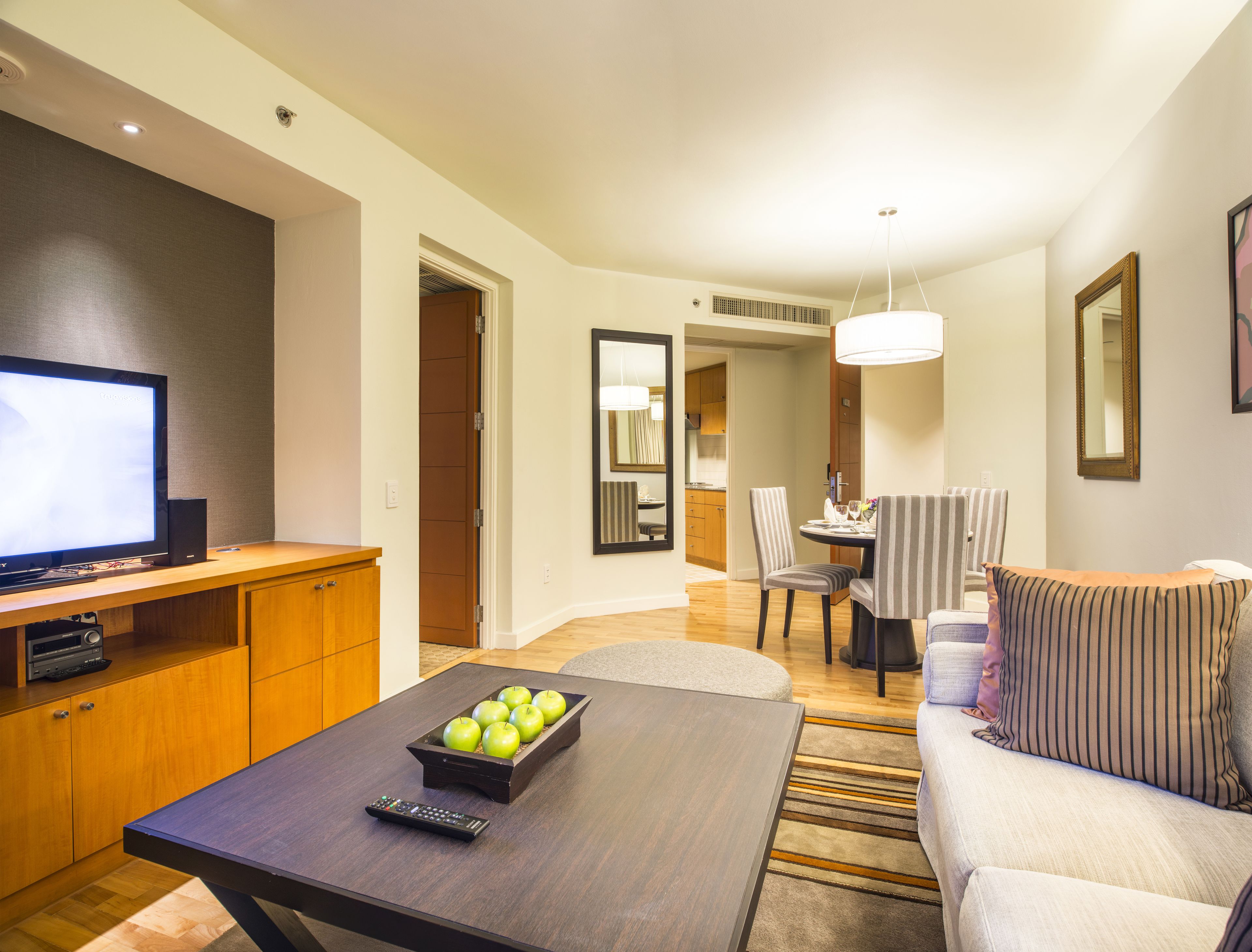 Una habitación de hotel moderna con televisor de pantalla plana, muebles de madera, zona de comedor y un rincón de estar acogedor.
