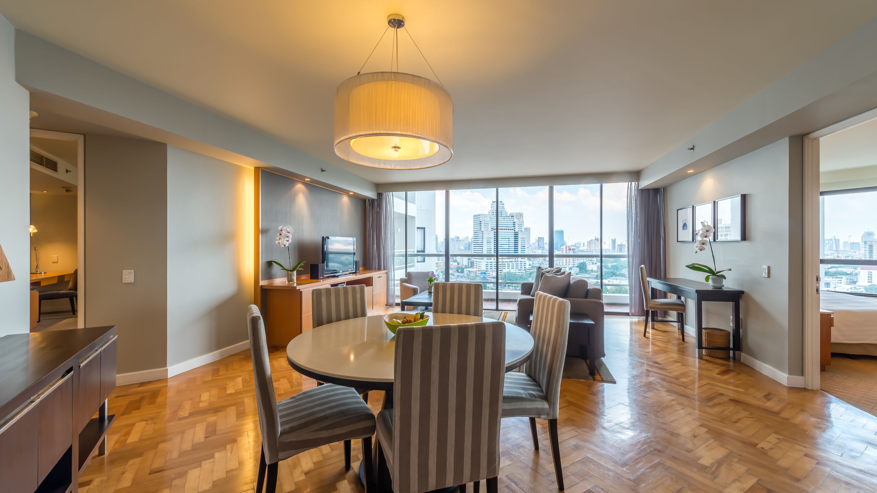A modern living room with a dining area, large windows offering a city view, and a chandelier.