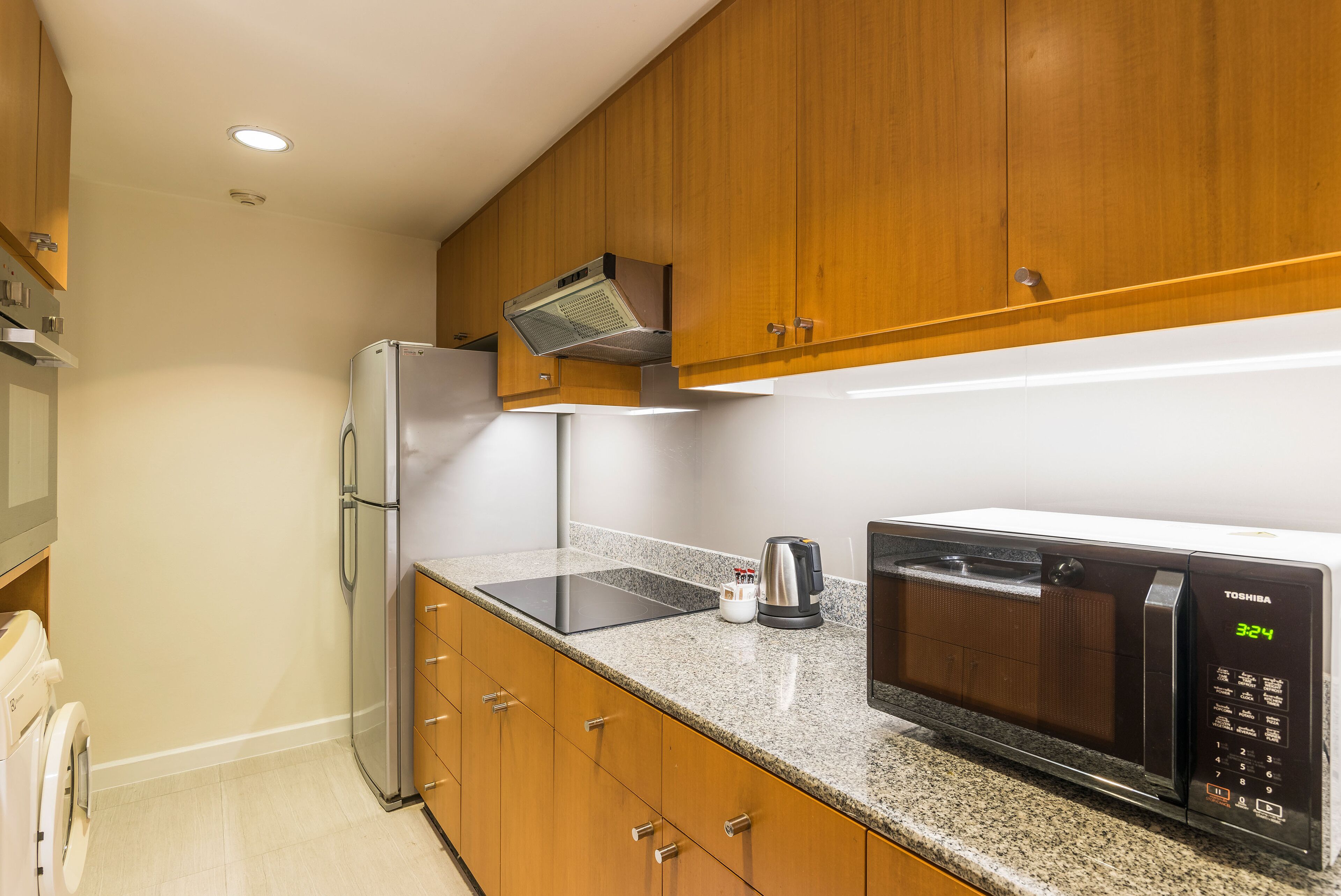 A kitchen with wooden cabinets, a stainless steel refrigerator, a microwave, and a built-in oven.