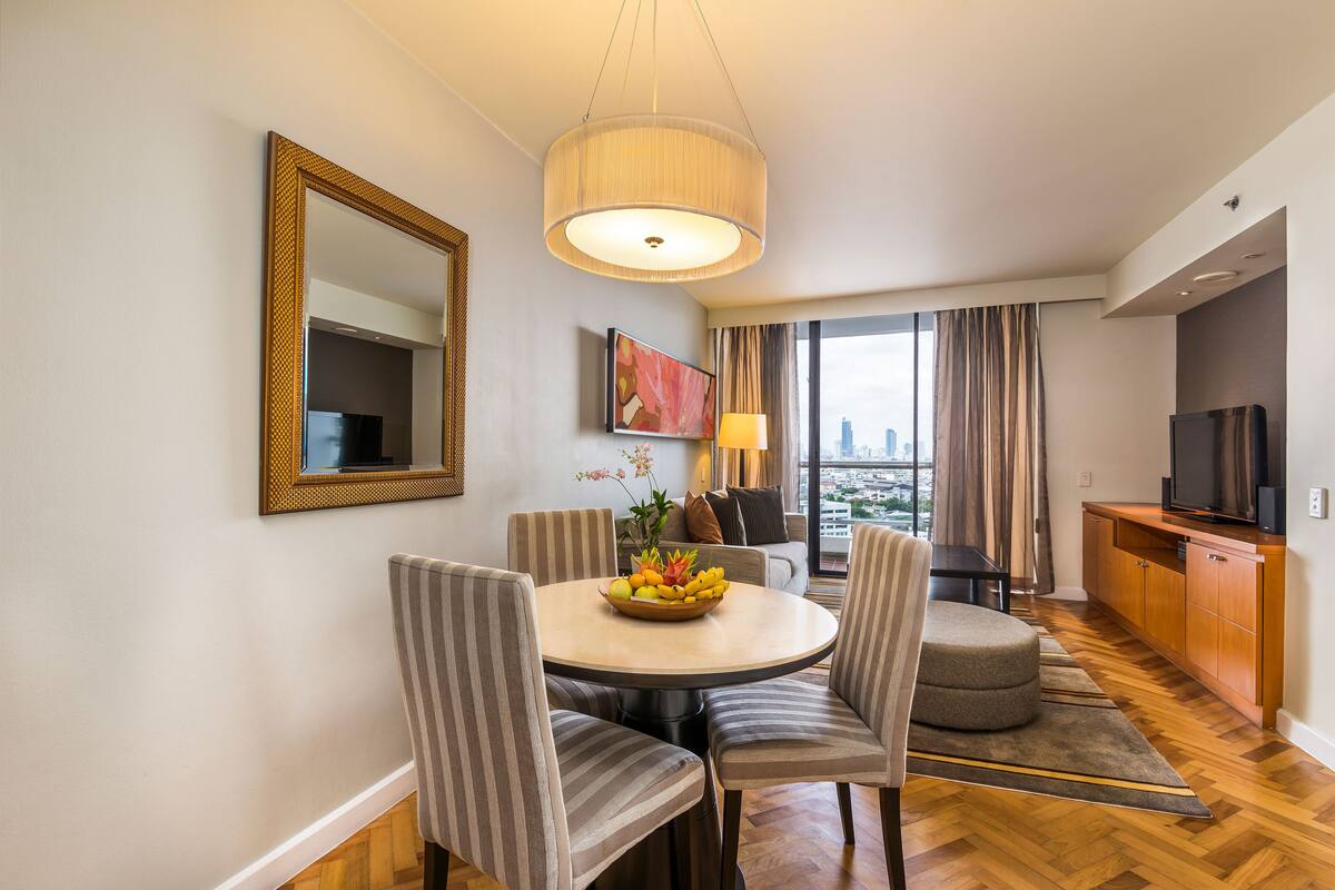 Ein modernes Hotelzimmer mit Essbereich, einem großen Spiegel, einem Fernseher und Blick auf die Stadt.