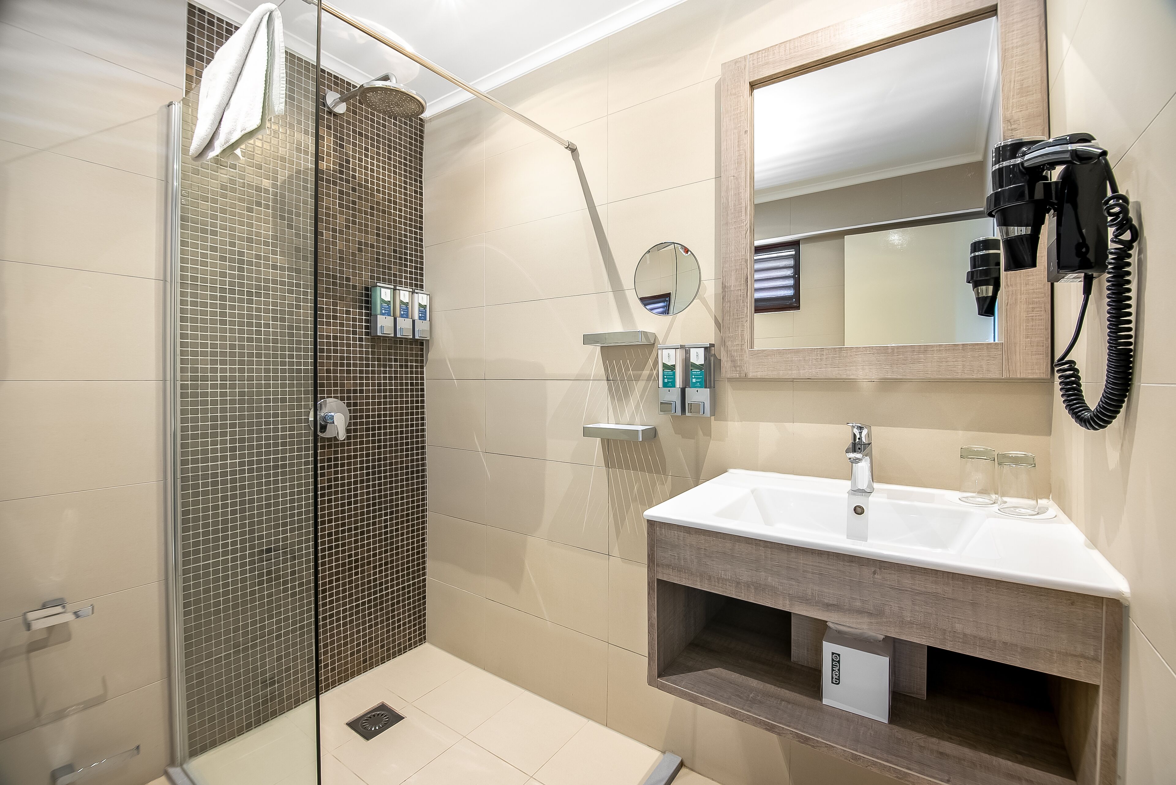 A modern bathroom with a glass-enclosed shower, a vanity with a mirror, and a hairdryer mounted on the wall.