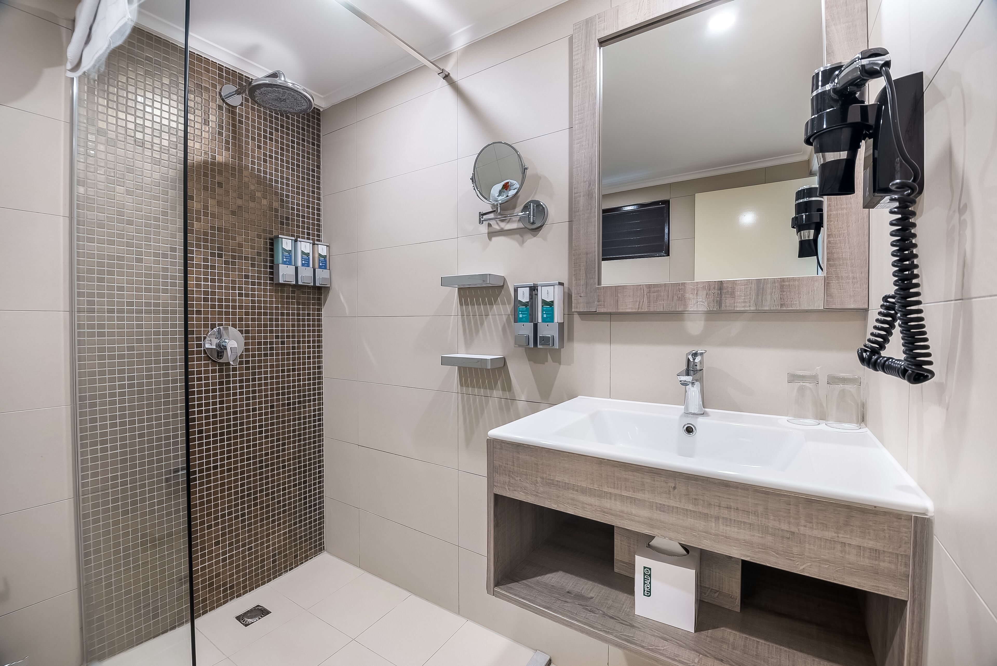 Casa de banho moderna com chuveiro, lavatório, espelho e secador de cabelo fixado na parede.