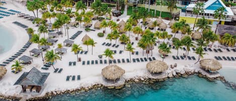 An aerial view of a resort with beachside accommodations, palm trees, and clear turquoise waters.