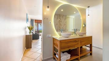 Een moderne badkamer met een houten wastafelmeubel, twee wasbakken en een grote spiegel met een ronde verlichting.