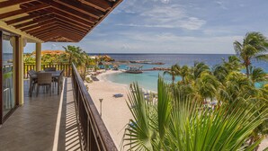 A balcony with a view of a beach and ocean, featuring a wooden pergola, outdoor seating, and palm trees. - LionsDive Beach Resort (Willemstad)