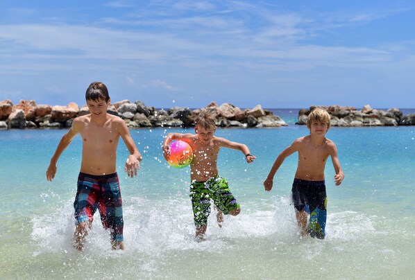 Three children playing in shallow water at a beach with rocks in the background.