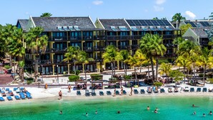 A resort with multiple-story buildings, a beach with sun loungers, and palm trees. - LionsDive Beach Resort (Willemstad)