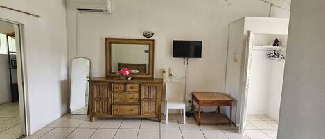 A room with a wooden cabinet, a white chair, a small table, a television, and a white wardrobe.