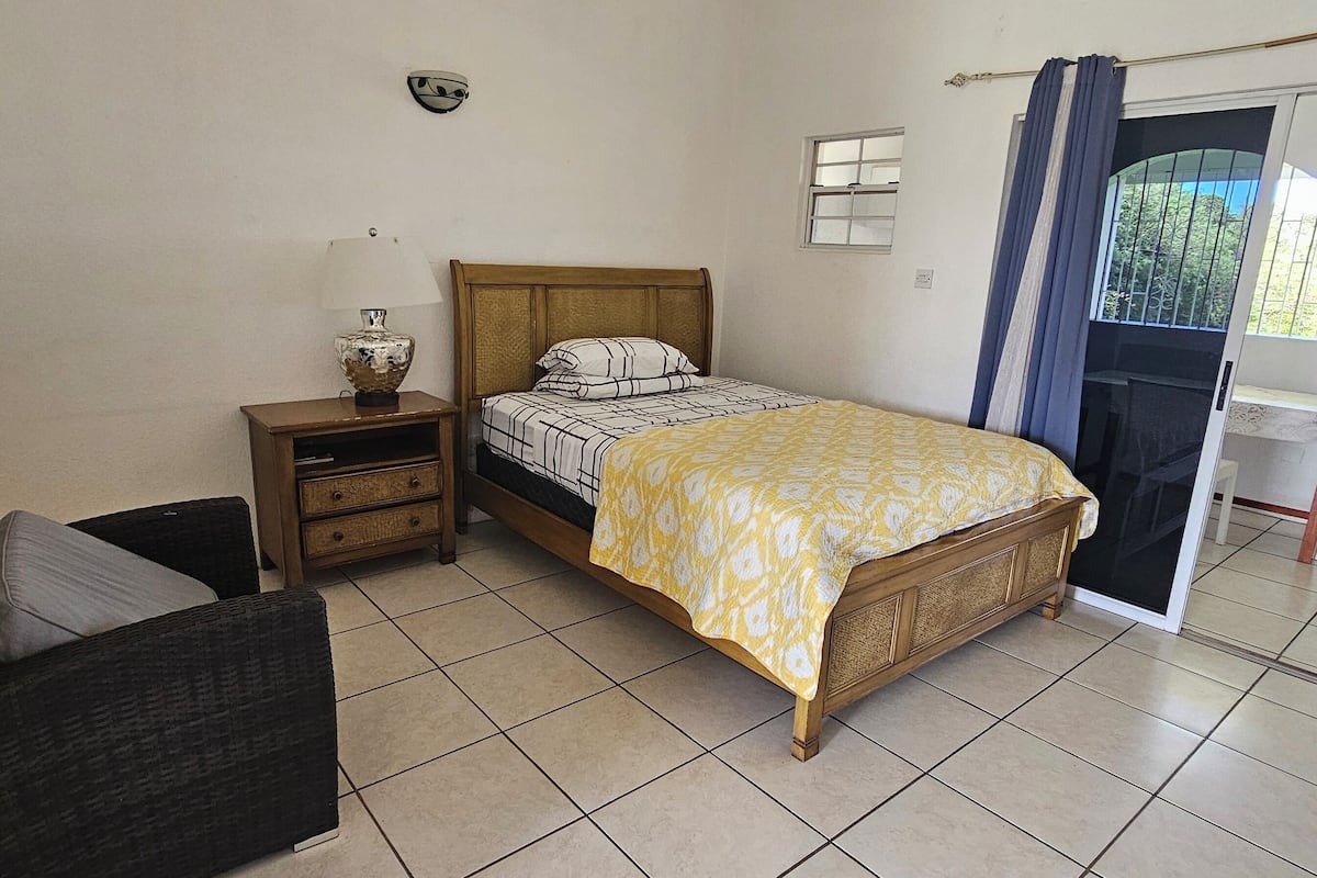A bedroom with a bed, nightstand, chair, and a window with curtains.