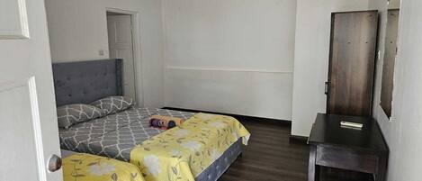 Una habitación con dos camas, suelo de madera, una puerta y una mesita con espejo.