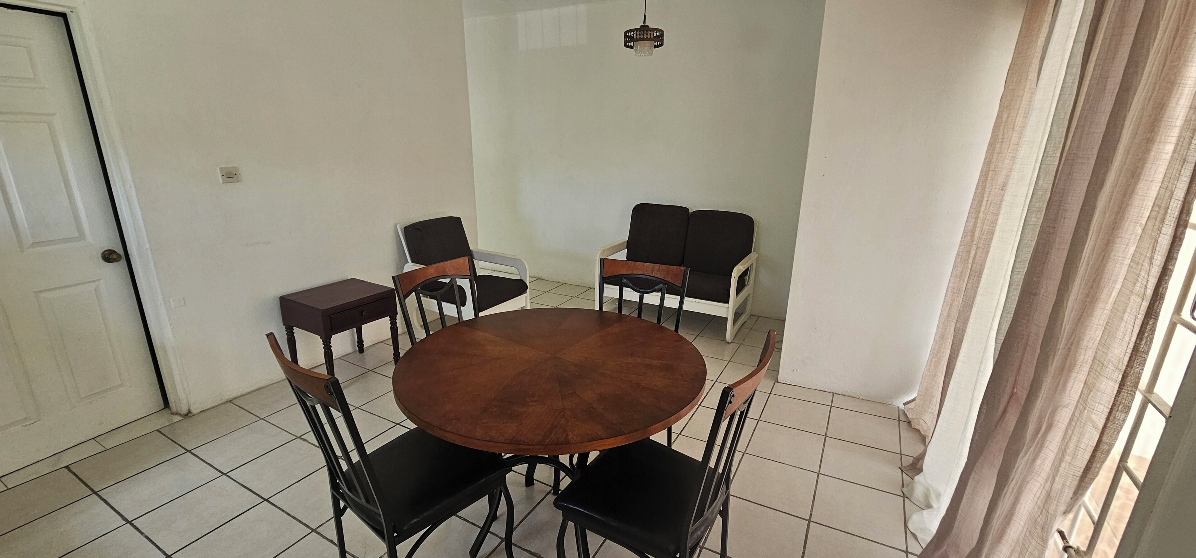 Un comedor con una mesa redonda y seis sillas, una puerta y una ventana con cortinas.