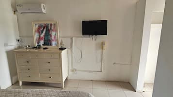 A small, well-lit room with a beige dresser, a flat-screen TV mounted on the wall, and a telephone.
