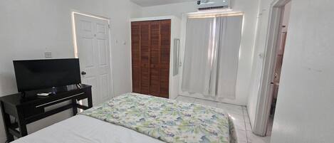 Ein Schlafzimmer mit einem Bett, einem Fernseher auf einem Schrank, einem Kleiderschrank und einem Fenster mit Vorhängen.