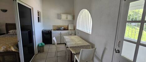 Habitación de hotel compacta con cama, kitchenette, mesa de comedor con sillas y ventana con vista a zonas verdes.