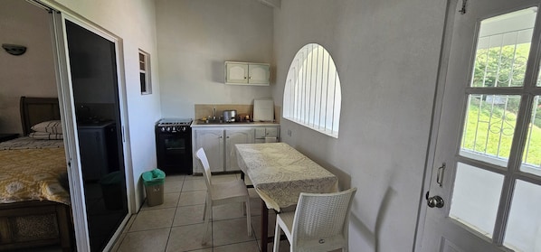 Une chambre d’hôtel compacte comprenant un lit, une kitchenette, une table à manger avec des chaises et une fenêtre donnant sur un espace verdoyant.