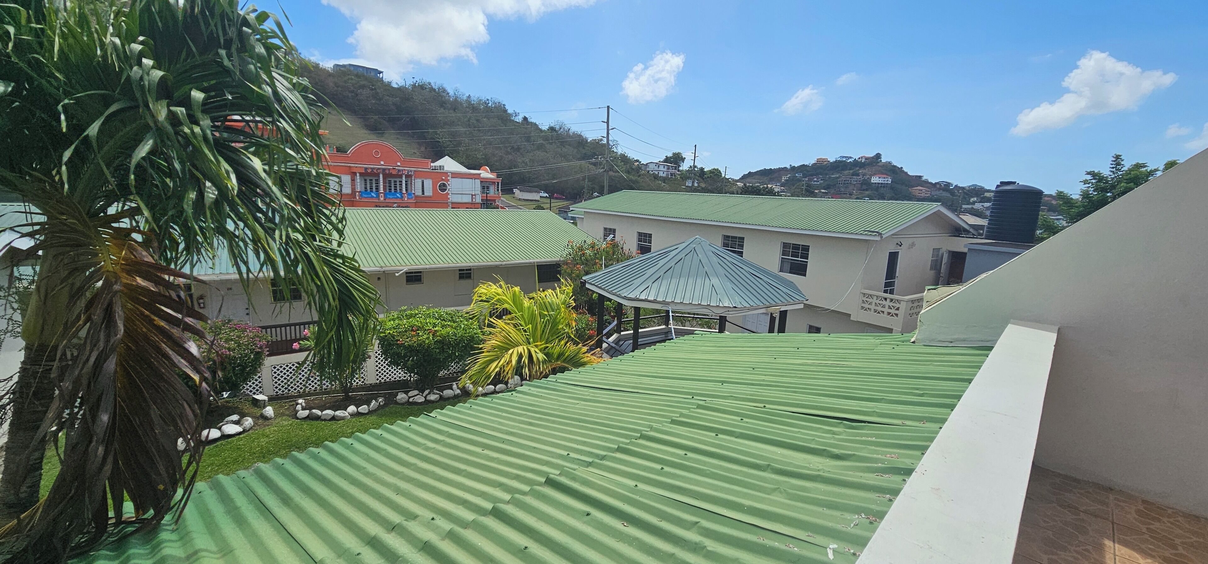 A residential area with houses, a green roof, and a hill in the background.