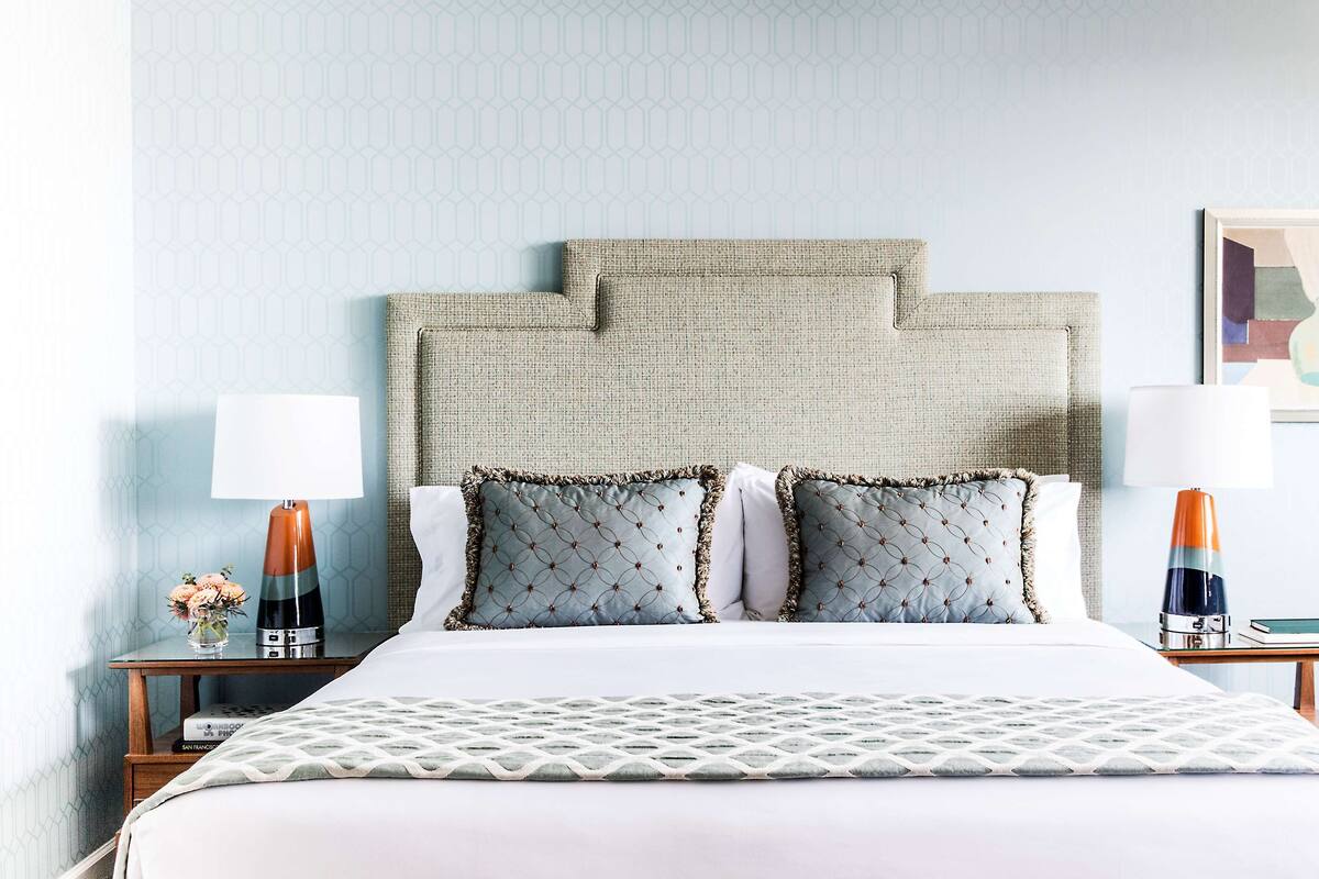A hotel room with a large bed, two bedside tables, a wall-mounted lamp, and framed artwork.