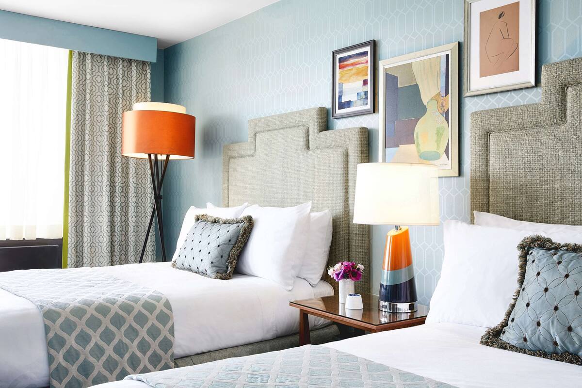 A hotel room with two beds, a nightstand, and a lamp.