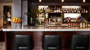 A bar area with a granite countertop, multiple liquor bottles, and black bar stools. - The Laurel Inn, part of JdV by Hyatt (San Francisco)