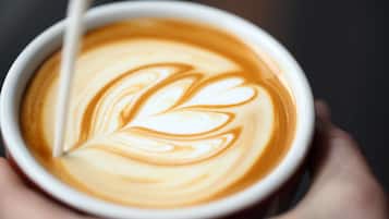 Een close-up van een hand die een koffiekop vasthoudt met latte-art.